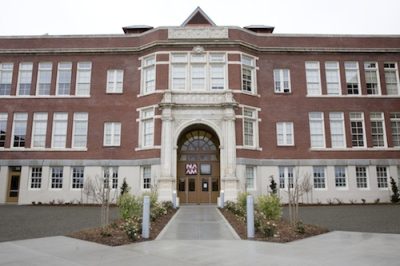 Multi-story red brick school building. In the window to the front entrance is a sign reading "N.A.A.M."