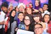 Group of people in a party photo booth wearing hats, feather boas, and smiling at the camera
