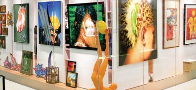 Storefront display featuring a variety of 2D, 3D, and multi-media artworks, some framed and hung on the wall, some sculptural and displayed on the platform below.