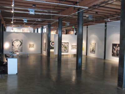 Empty gallery space with white walls and industrial metal beams in the center of the room. 2D work is hung on the walls.