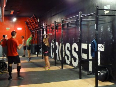 People using crossfit equipment in a gym. White text across a black wall in the background reads "CROSSFIT"