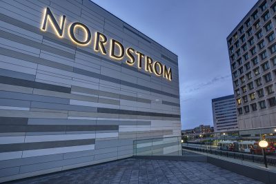 Backlit metal lettering on the side of a modern grey building reads "Nordstrom"