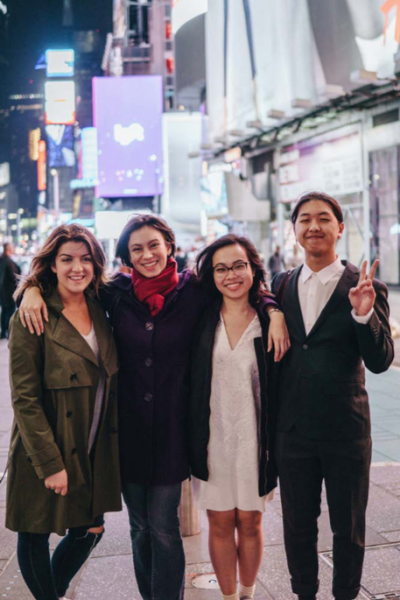 Four smiling college students standing with their arms around each other in New York's Times Square