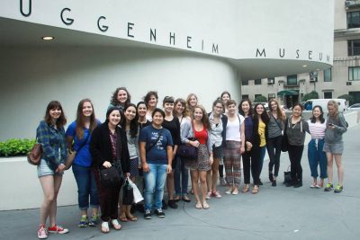 Group of youths stand outside the Guggenheim Museum entrance, all smiling at the camera.