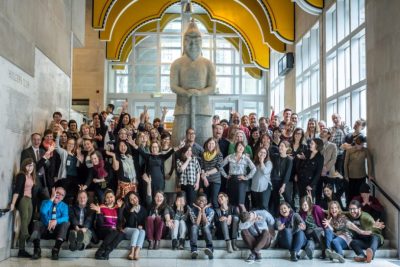 Group staff photo in front of a bright, windowed museum foyer featuring a large sculpture of a figure in stone.