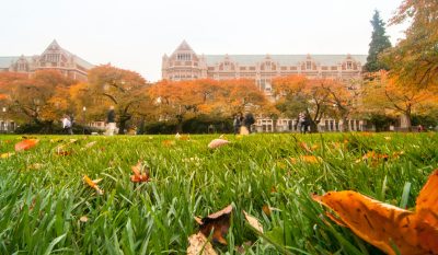 University buildings, with autumnal trees and grass in the foreground.