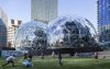 Glass geodesic dome structures in front of a set of skyscrapers.