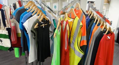 Clothing rack holding different t-shirts, tank tops, sweat shirts, and safety vests.