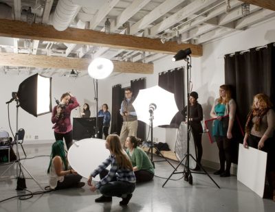 Brightly lit photo studio full of different people supporting a photo shoot.