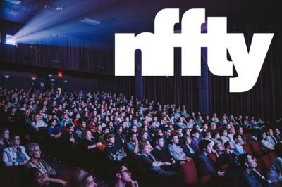 Crowded, darkened movie theater with a view of the audience and the projector booth. White bold sans serif text in the upper right corner reads "nffy"