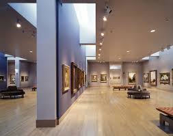 Brightly lit art gallery with paintings on the walls and benches in the center of the room