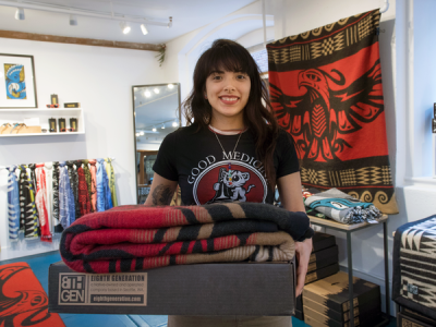 Young retail worker stands in a shop setting full of textiles and goods designed by Indigenous artists