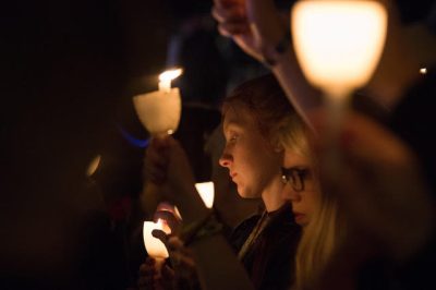 People gathered in a dark setting holding a candlelight vigil.