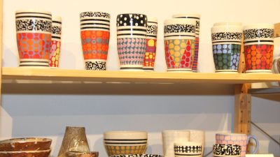 Shelf full of brightly colored, patterned ceramics tumblers and mugs.