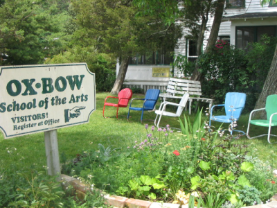 Garden in front of a white clapboard house, a sign that reads "Oxbow School of the Arts" out front.