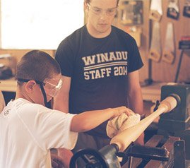 Instructor watches over a youth using a piece of woodturning equipment in a studio setting.