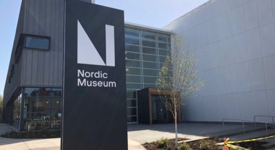 Exterior of a concrete and glass modern art building. A tall metal sign out front reads "Nordic Museum."