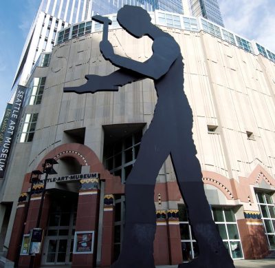 a large metal sculpture depicting a human form hammering a piece of metal stands in front of the Seattle Art Museum
