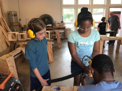 two youths work together with an older individual on a woodworking project