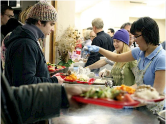 People being served in a busy cafeteria line by smiling and chatting cafeteria workers.