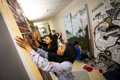 Young adults work together on large art murals in a studio setting.