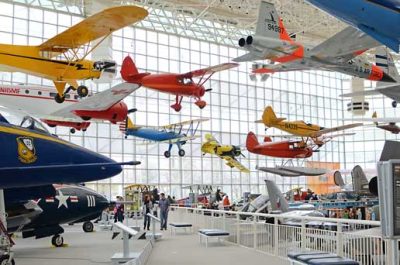 Large, light filled airplane hanger turned museum, with display airplanes hung from the rafters and stationed on the ground.