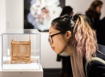 Young femme adult wearing glasses looks at an art object in a glass vitrine.
