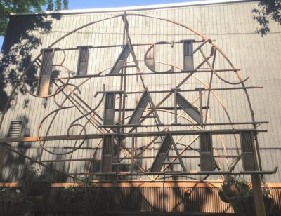 Metal black and bronze sign reading "Black & Tan Hall" in ornate script lettering, against a backdrop of a grey slated wall.