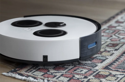 A white and black domestic vacuum robot rests at the edge of an ornate floor rug.