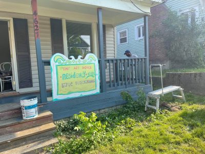 Front porch of a house with a colorful sign out front that reads "Tiny Art House Residency Center BIPOC Sustainable"