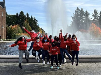 Group of students in front of a university fountain, all wearing match red shirts, leaping into the air and smiling