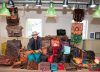 Person wearing a leather hat stands behind a market table display of leather goods and bags.