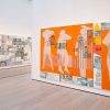 Museum gallery with bright oange art work featuring human figures.