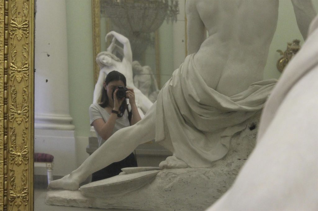 A picture of a woman taking a photograph of a sculpture, reflected in a mirror