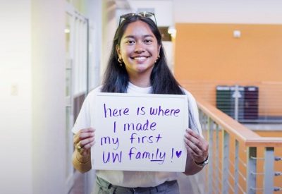 A student holding a sign that says "here is where I made my first UW family!" for our Home Away From Home Campaign that asks why students love the Kelly ECC