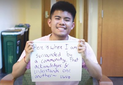 A student holding a sign that says "Here is where I am surrounded by a community that acknowledges & understands one another ~ uwu." for our Home Away From Home Campaign that asks why students love the Kelly ECC