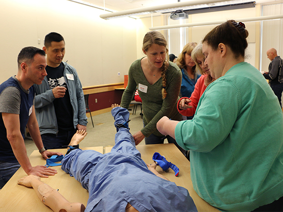 Participants observe an instructor demonstrating how to use a tourniquet to control bleeding.