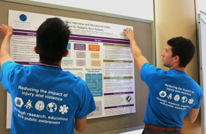 Two students in blue HIPRC T-shirts hang a research poster on a display board.
