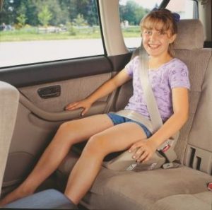 A child seated in a no-back booster seat, with the seat belt correctly positioned low over the hips and across the center of the shoulder.