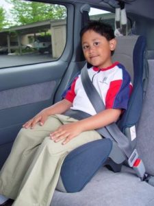 A child in a high-back booster seat, with the seat positioning the seat belt correctly over the lower hips and the center shoulder.