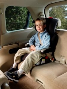 A child seated in a high-back booster seat with seat belt fastened.