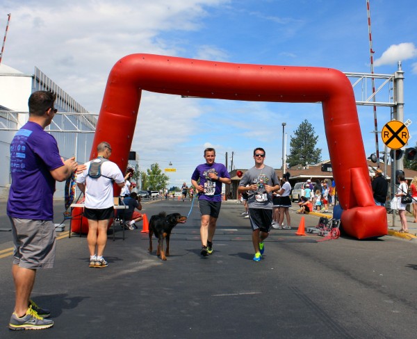 Aaron Newton (class VP), Chris Varady (class P), and Sterling the dog passing the finishing line together after running the 12K.
