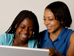 Mother and daughter are sitting in front of laptop smiling.