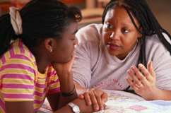 Mother is sitting, touching daughters hand while talking to her.