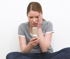 Girl looks at phone, while putting her hand to her face in horror.