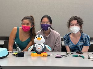 Three girls sitting next to an adapted penguin toy