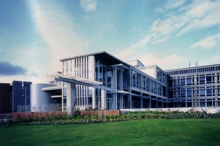Modern metal and glass university building, with a green well maintained lawn in front.