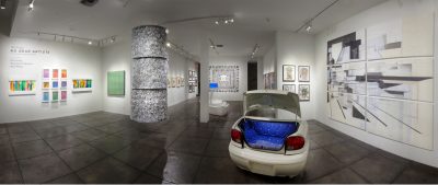 Modern art gallery with white walls and a polished concrete floor. Artwork consists of drawings and paintings hung on the walls, as well as some video, installation, and sculptural work in the middle of the space.