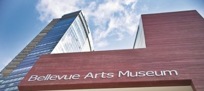 Modern red stone facade of an art museum. Silver sign lettering on the wall reads "Bellevue Arts Museum"