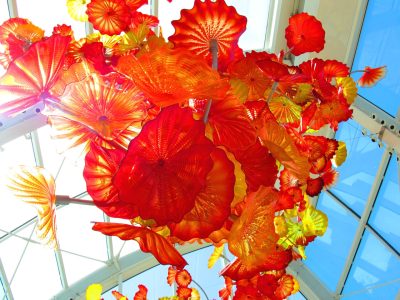 Red, orange, and yellow glass sculpture featuring smaller blown glass elements installed together to create a large ceiling installation.
